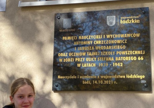 Uczennica klasy 8b stoi obok tablicy upamiętniającej bohaterów walki o polską szkołę.
